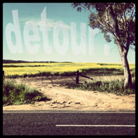 A bitumen road in the foreground with a dirt road leading to a gate. The text 'detour?' appears subtly in the sky. A bitumen road in the foreground with a dirt road leading to a gate. The text 'detour?' appears subtly in the sky.