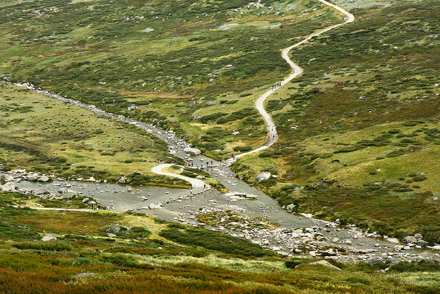 The snowy ricver runs through a green valley. White and grey rocks surround the river. A walking trackign winds down the side of the mountain towards the river, The snowy ricver runs through a green valley. White and grey rocks surround the river. A walking trackign winds down the side of the mountain towards the river,