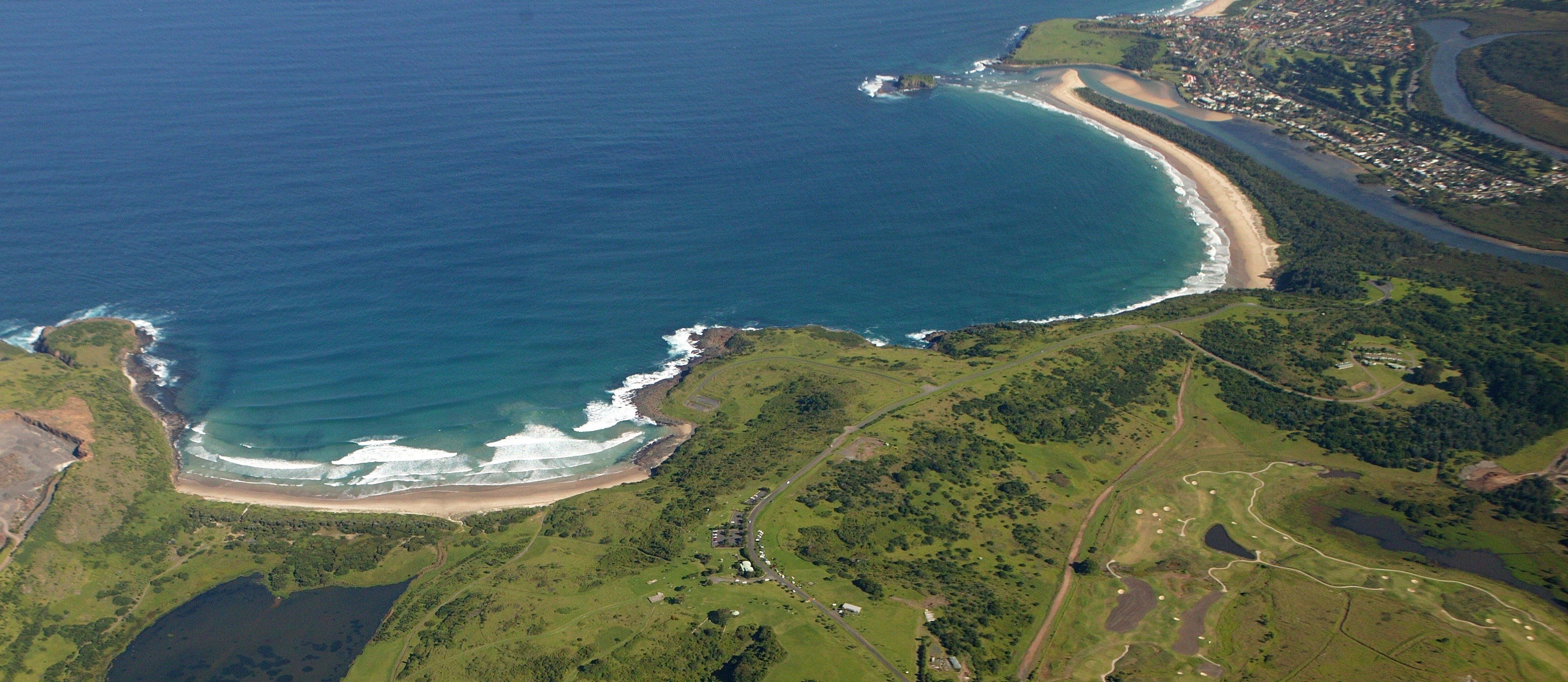 Aerial view of the coastline with deep blue sea, white sandy beaches, some rocky areas and then grassy land behind the beach. Aerial view of the coastline with deep blue sea, white sandy beaches, some rocky areas and then grassy land behind the beach.