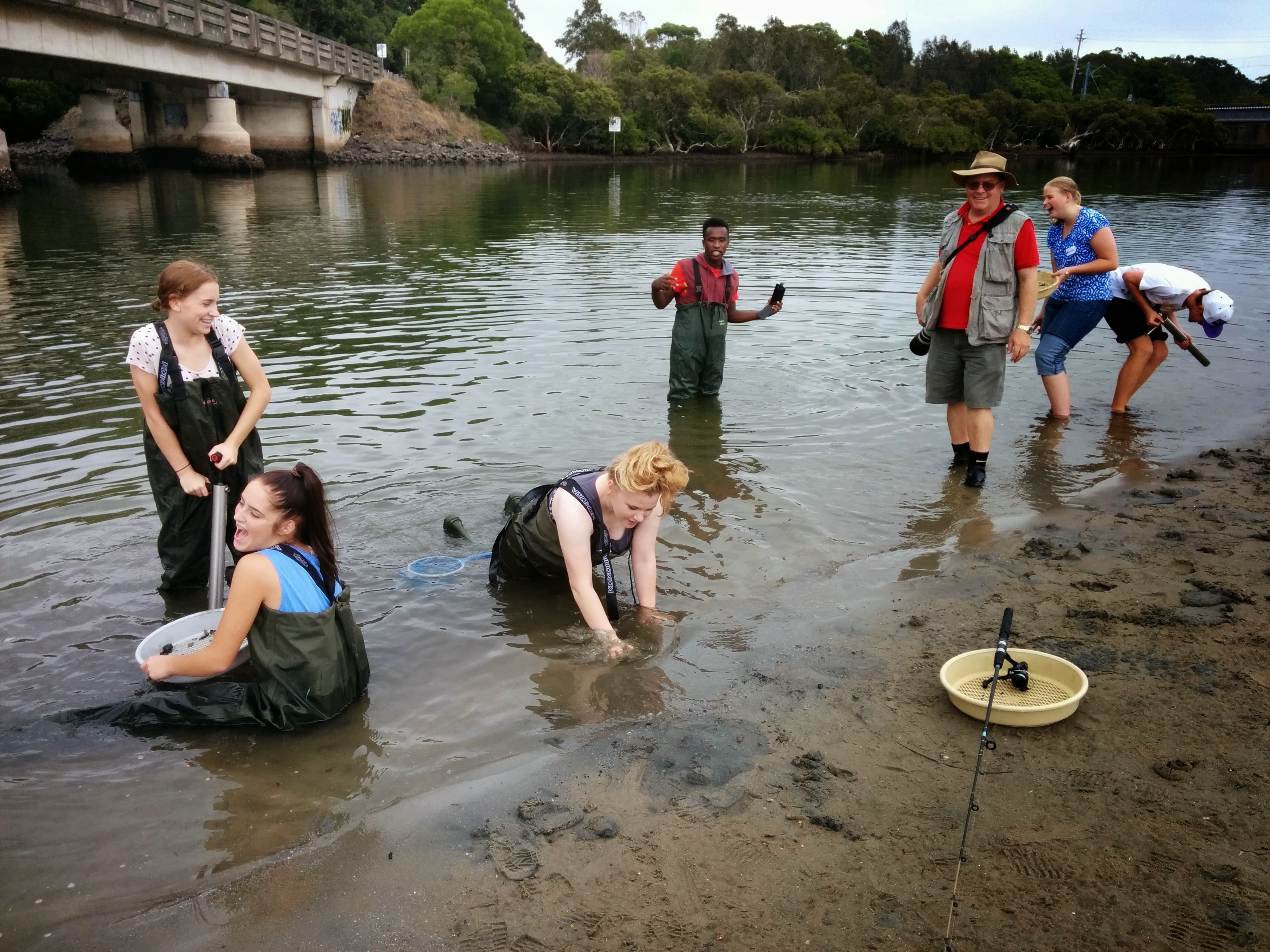 A group of older students wearing protective wading gear are working in the muddy water, they are laughing and having fun. A group of older students wearing protective wading gear are working in the muddy water, they are laughing and having fun.